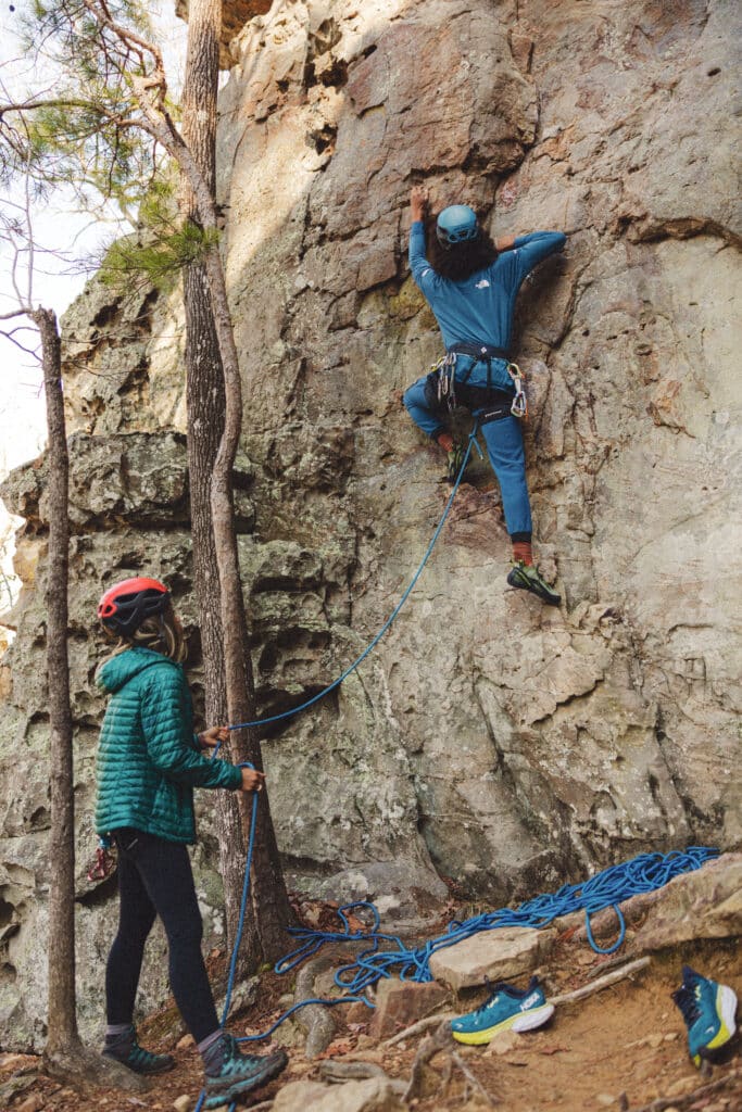 A person belaying another person lead climbing a rock.